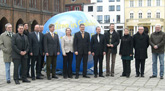 Das Foto zeigt eine Gruppe von Menschen auf dem Alten Markt in Stralsund, sie stehen vor einem bermannsgroen blulich-weien Ballon. Es handelt sich um den frisch einberufenen Klimarat am 30.3.2009.