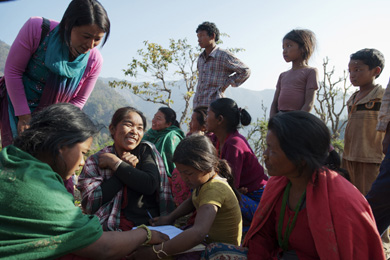 Das Foto zeigt eine Gruppe Menschen in einer bergigen Landschaft. Im Mittelpunkt des Geschehens stehen drei Frauen und ein Mädchen, die sich ein Buch ansehen.
