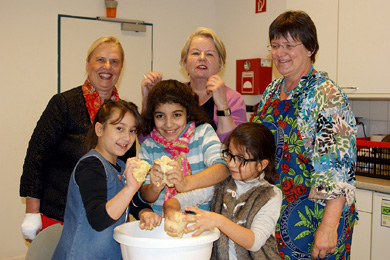 Das Foto zeigt drei Kinder und drei Lehrerinnen mit einer Schüssel voller Teig.