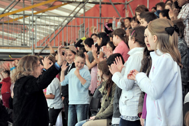Das Foto zeigt viele singende Kinder in einem Stadion.