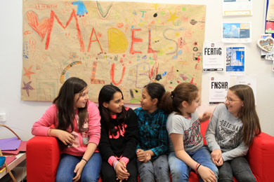 Das Foto zeigt Mädchen, die auf einem Sofa sitzen. Im hintergrund ein Poster mit der Aufschrift Mädels-Club.
