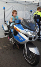 Das Foto zeigt ein Mädchen, das sehr zufrieden auf einem Polizeimotorrad sitzt.