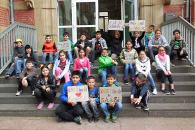 Das Foto zeigt Kinder, die auf der Treppe vor ihrer Schule sitzen und Plakate zur Schokofair-Aktion inden Händen halten.