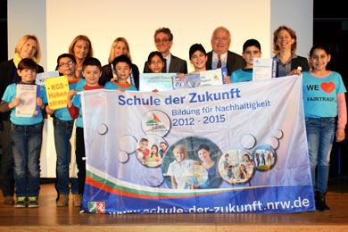 Das Foto mehrere Schüler und ihre Lehrer, die auf einer Bühne stehen und eine Fahne halten. Auf der Fahne steht Schule der Zukunft.