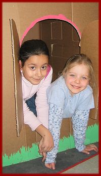 Zwei Schülerinnen schauen aus selbstgebauten Pappfenster