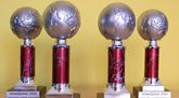 Das Foto zeigt vier Pokale in Form von Weltkugeln