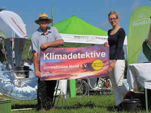 Das Foto zeigt den Bürgermeister und die Mitarbeiterin der Bioenergieregion Rügen vor einem Solarkocher, mit einem Klimadetektive-Transparent