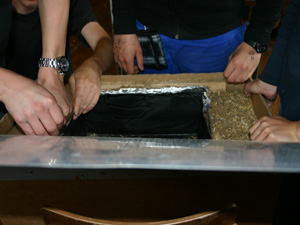 Das Foto zeigt mehrere Hände beim Arbeiten - Jugendliche bauen eine Solar-Kochkiste.