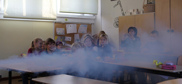 Das Foto zeigt Schüler in einem Klassenraum; quer durch den Raum schießt ein dicker Strahl von Nebel.
