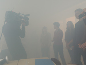 Das Foto zeigt einen stark vernebelten Klassenraum mit Schülern und einem Kamerateam.