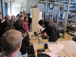 Das Foto zeigt einen Mann, der - inmitten eines großen Labors - Schülern ein Experiment zeigt.