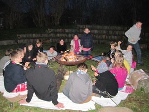 Das Foto zeigt Jugendliche, die um ein Feuer herum sitzen und Stocjbrot backen.