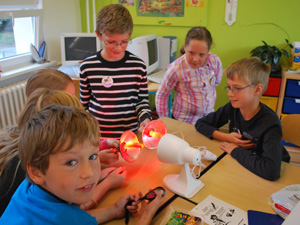 Das Foto zeigt Schülerinnen und Schülern, die mit einer Rotlichtlampe und kleinen Reflektoren experimentieren.