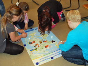 Das Foto zeigt vier Schülerinnen bzw. Schüler, die auf dem Fußboden sitzen und kleine Bildkärtchen auf einer Landkarte der Insel Rügen anbringen.