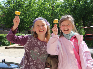 Das Foto zeigt zwei Mädchen, die gedünstete Maisscheiben halten und sich sehr darüber freuen.