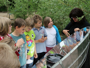 Das Foto zeigt einen Solarkocher, einige Kinder und eine dunkel gekleidete Frau, welche den Kindern den Solarkocher erklärt.