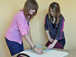 Das Foto zeigt zwei Mädchen, die an einer auf dem Tisch liegenden Landkarte arbeiten.