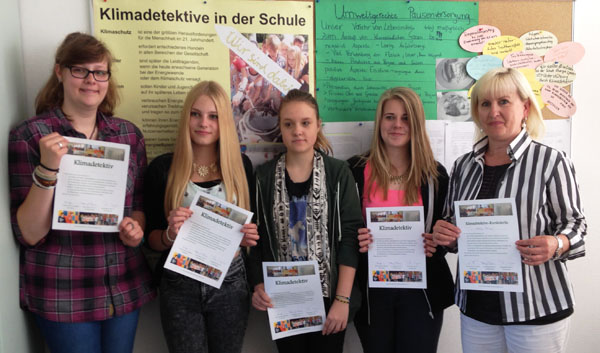 Das Bild zeigt vier Schülerinnenmit ihrer Lehrerin. Sie stehen vor einem Poster der Aktion Klimadetektive in der Schule des UMweltbüro Nord e.V. und halten Urkunden in den Händen, die ihre erfolgreiche Teilnahme am Projekt bescheinigen.