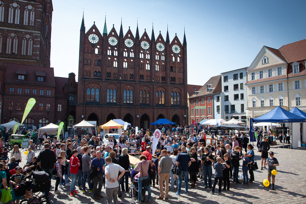 Das Foto zeigt den Stralsunder Marktplatz mit dem Rathaus. Auf dem Markt stehen viele Menschen und schauen beim 6. Stralsunder Solarbootrennen zu.