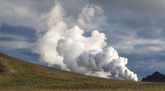 Das Foto zeigt die Geothermalregion Krafla auf Island. Es ist eine karge Graslandschaft zu sehen; in der Bildmitte steigt weißer Dampf auf.