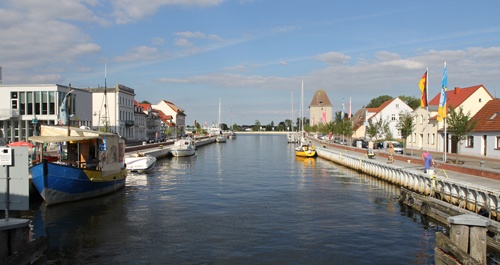 Das Foto zeigt die Uecker, die durch die Stadt Ueckermünde fließt; links im Bild das Rathaus.