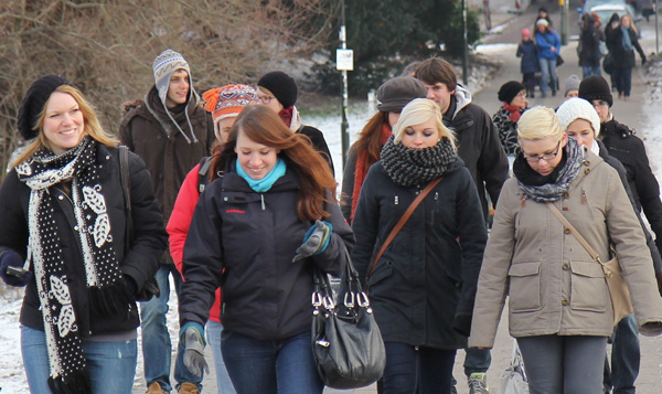 Das Foto zeigt eine Gruppe junger Menschen in Winterkleidung, die durch eine städtische Grünanlage gehen.