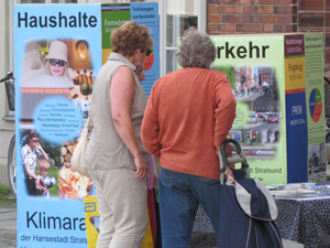 Rentnerinnen betrachten mannsgroe Quader, die mit Informationen zu den Quellen der CO2-Emissionen der Hansestadt Stralsund beschriftet sind. Die Quader sind unterschiedlich gro, ihr Volumen steht fr den Anteil der jeweiligen Quelle an den Emissionen.