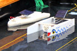 Das Foto zeigt zwei kleine Boote - Katamarane - die aus Schaumpolystyrol gebaut wurden und jeweils mit einer Solarzelle, einem Motor und einer Schiffsschraube als Antrieb ausgestattet sind.