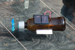 Das Foto zeigt ein kleines Boot, das aus einer braunen Plastikflasche gebaut wurde und mit einer Solarzelle, einem Motor und einer Schiffsschraube als Antrieb ausgestattet ist.