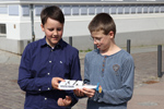 Das Foto zeigt zwei Schüler, die ein kleines Modellboote - ein Solarboot - präsentieren.