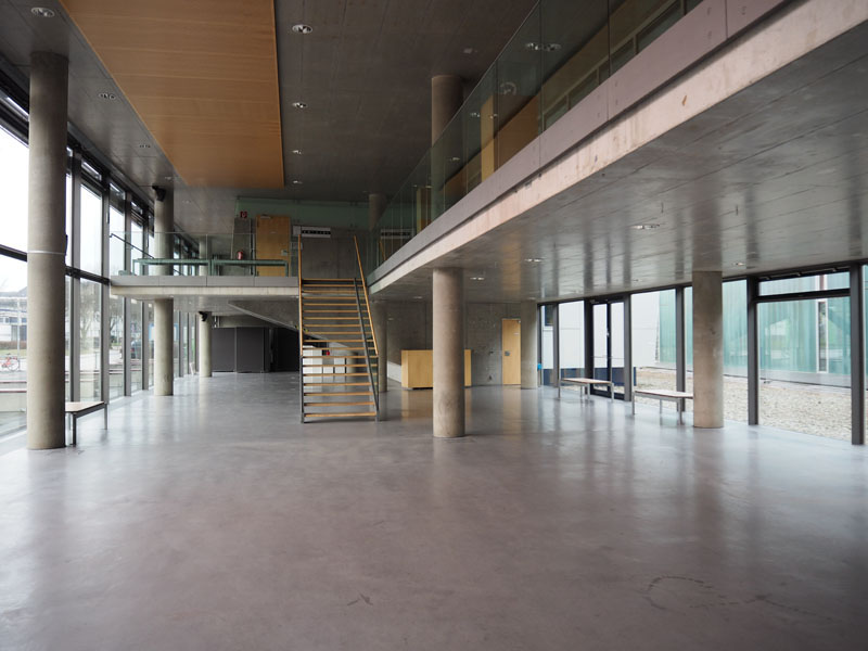 Das Foto zeigt das Foyer der Fakultät für Architektur - Design - Innenarchitektur der Hochschule Wismar - einen großen Raum aus Beton mit hellen Fensterfronten.