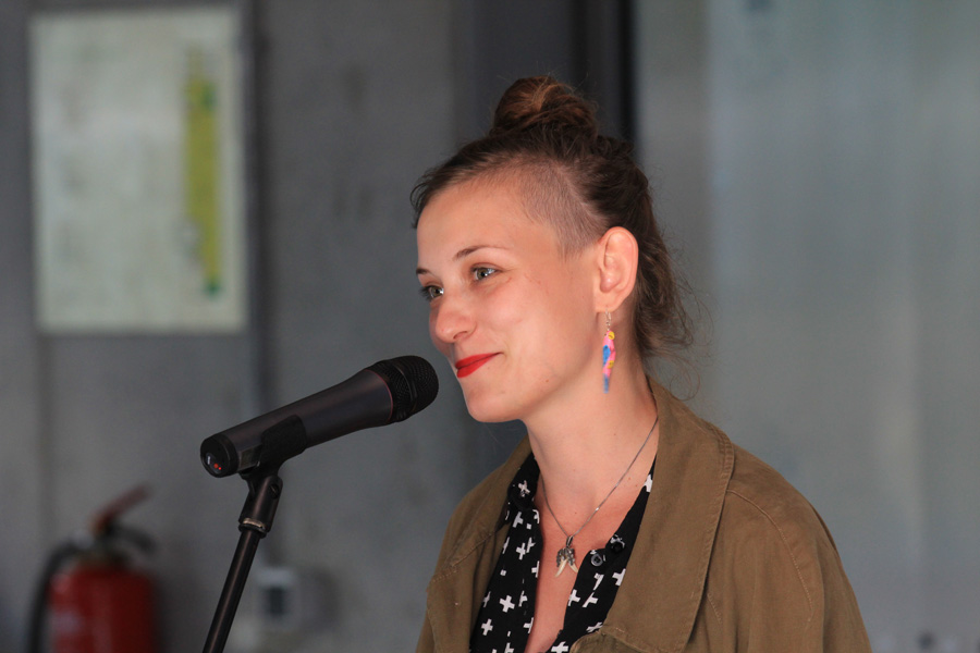 Das Foto zeigt das Brustbild einer jungen Frau, die in ein Mikrofon spricht.