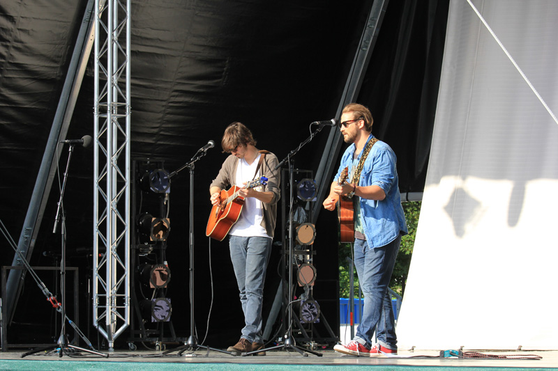 Das Foto zeigt zwei Männer, die auf einer Bühne stehen, singen und dazu Gitarre spielen.