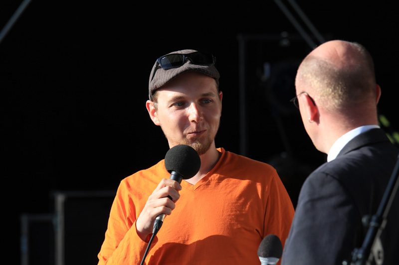Das Foto zeigt zwei Männer, die auf einer Bühne mit Mikrofonen stehen und sich unterhalten.