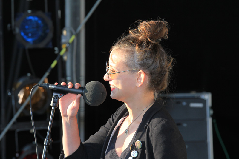 Das Foto zeigt eine Frau, die auf einer Bühne steht und in ein Mikrofon spricht.