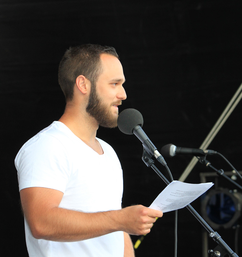 Das Foto zeigt einen Mann, der auf einer Bühne steht und in ein Mikrofon spricht.