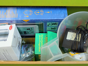 Das Foto zeigt eine Box mit einem offenen Schubfach, darin u.a. ein Digitalthermometer, ein Messbecher und weitere Materialien zum Messen, Experimentieren und Lernen.