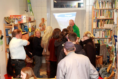 Das Foto zeigt einige Menschen, die in einem Raum mit vielen Bücherregalen stehen und sich angeregt unterhalten.