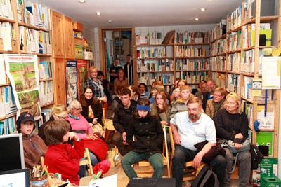Das Foto zeigt einen Bibliotheksraum, in dem ca. 20 Menschen sitzen und sich einen Vortrag anhören.