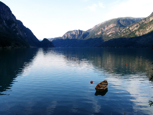 Das Foto zeigt einen stillen See in einer bergigen Landschaft. Im Vordergrund schwimmt ein kleines Ruderboot.