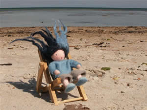Das Foto zeigt eine kleine Puppe - den Wassermann Aquarius - im Strandkorb vor einem Gewässer sitzen.