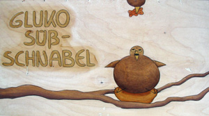 Das handgemalte Bild zeigt ein dickes Vogelkind im Nest; vom oberen Bildrand her kommt eines seiner Eltern mit einem Gummibärchen im Schnabel.